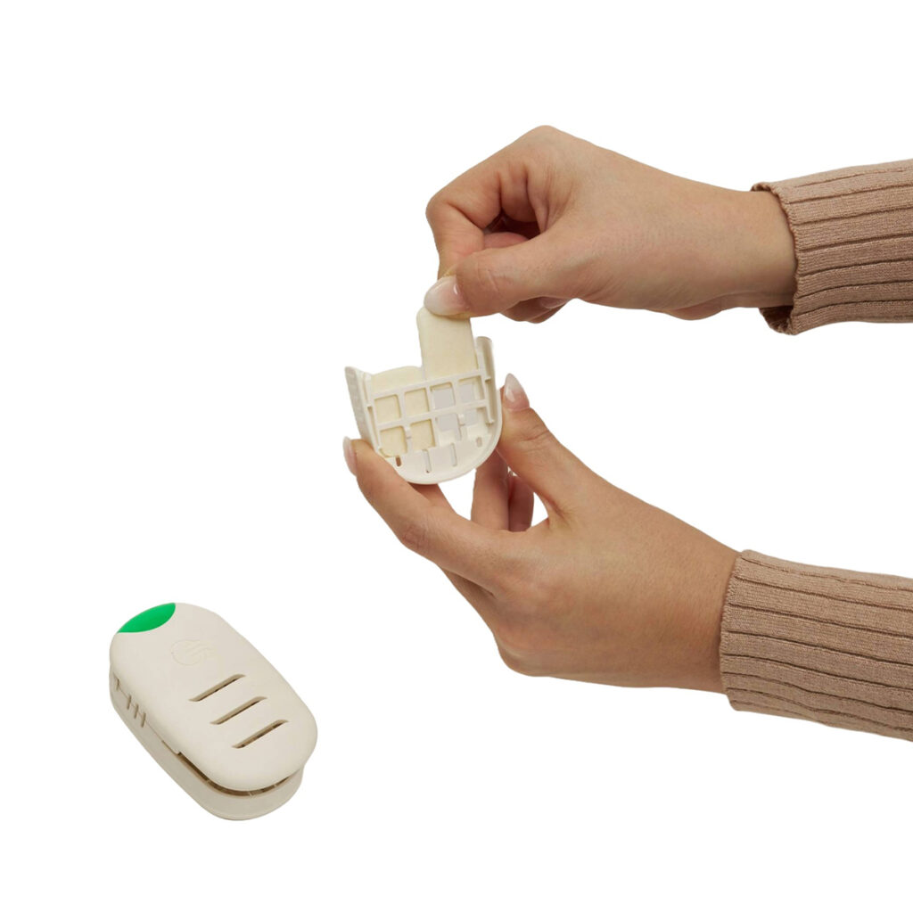 Two hands insert a white rectangular piece into a curved plastic holder. A small white device with a green button is placed nearby on a white background.