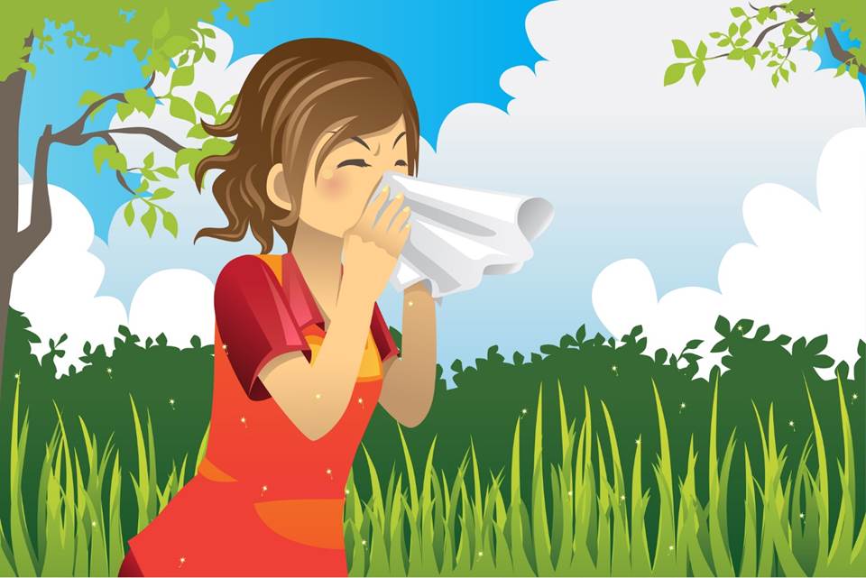 A girl wearing a red dress stands outdoors in tall grass, sneezing into a white tissue. The sky is blue with clouds, and green trees and bushes are in the background.